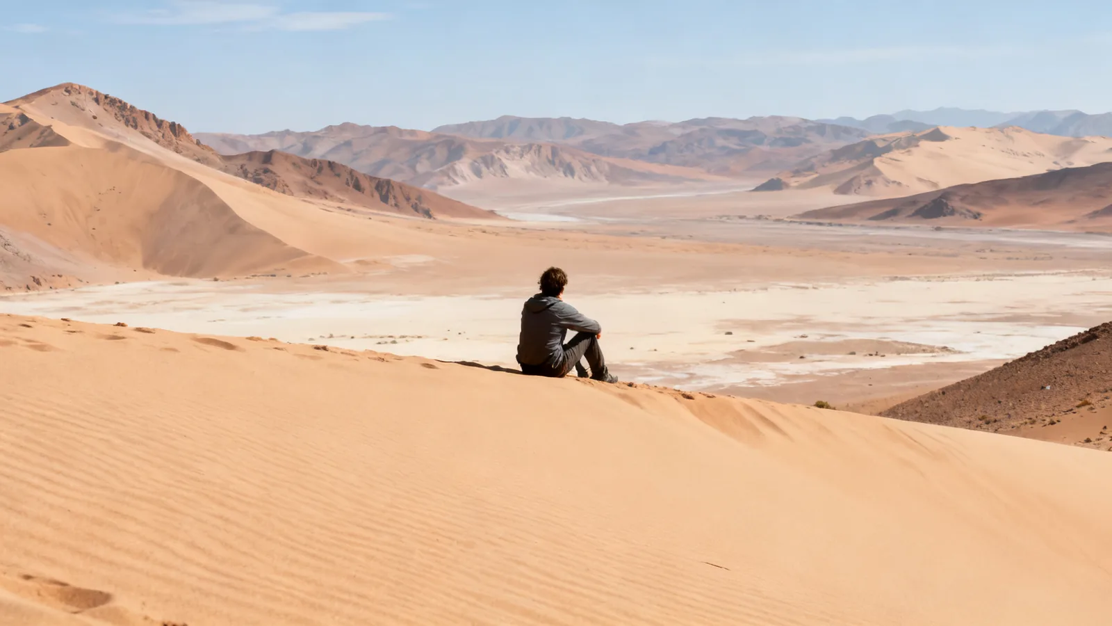 A distant traveller sitting on a desert dune, photographic illustration